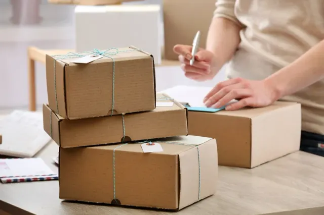 Caixas de papelão amarradas e etiquetadas, prontas para o envio, enquanto uma pessoa preenche o formulário de entrega