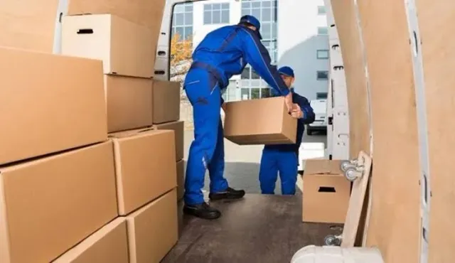 Dois ajudantes uniformizados carregando caixas de papelão dentro do caminhão baú